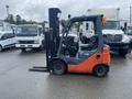A 2011 Toyota 028FG15 forklift with an orange and black body positioned to the side with its forks lowered and wheels on wet pavement