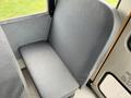 A gray upholstered bus seat is shown with no one sitting on it, positioned inside a vehicle designed for public transportation