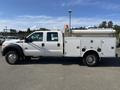 A 2015 Ford F-450 SD truck with a white exterior, equipped with an orange warning light on the roof and a utility bed featuring compartments and tools on the side