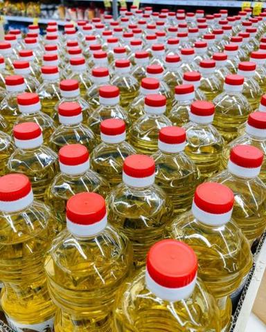 Bottles of various cooking oils including sunflower oil, rapeseed oil, soybean oil, olive oil, peanut oil, and palm oil with red caps arranged in a store display