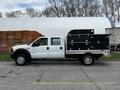 A white 2007 Ford F-550 with a black utility bed and multiple compartments on the side is parked on a street