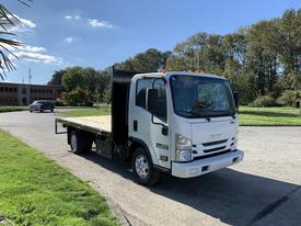 A 2015 Isuzu NPR truck with a flatbed design facing forward and a black cargo area with bright orange lights on top