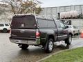 A gray 2015 Toyota Tacoma with a cap on the truck bed and chrome accents parked on a wet surface