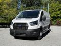 A 2023 Ford Transit van in white with a black grille and fog lights parked prominently in a well-lit area
