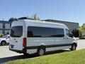 A 2023 Mercedes-Benz Sprinter van with a sleek design featuring large windows and a high roof, parked on grass, showcasing its modern silhouette and rear taillights