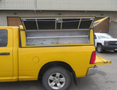 A yellow 2015 RAM 1500 pickup truck with an open truck bed cap revealing a wooden interior and a partially raised tailgate