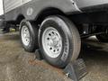 Close-up of two tires from a 2022 Aspen Trail trailer with a black tread pattern secured on chocks with a chain attached to the ground