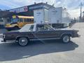 A 1982 Mercury Grand Marquis in a dark color with a white vinyl roof and chrome trim parked on a street with a school bus visible in the background