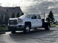 A white 2017 GMC Sierra 3500HD pickup truck with a flatbed and chrome accents parked on a roadway