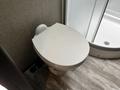 A white toilet with a round lid sits on a floor with light-colored wooden tiles