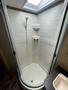 A compact shower stall featuring a curved glass door a detachable showerhead and tile walls in a white finish