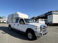 A 2014 Ford F-350 SD pickup truck with a white camper shell in the bed parked in a lot showcasing its crew cab and chrome front grille