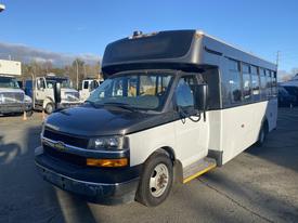 A 2018 Chevrolet Express bus with a black front and white body showing multiple windows on the side and a gray roof