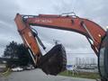 A 2006 Hitachi ZX200LC excavator with an orange arm and a large metal bucket positioned for digging