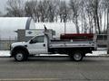A white 2008 Ford F-450 Super Duty truck with a flatbed and a red tool box in the back parked on the street