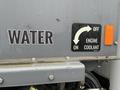 A close-up of a 2023 Mack Granite truck showing a water label and a sign with arrows indicating the positions for engine coolant on and off