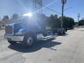 A blue 2008 Peterbilt 340 truck with a spacious cab and a long chassis parked on the street with bright sunlight reflecting off its surface