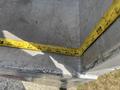 A tape measure on a concrete surface showing measurements near a corner of a structure