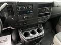 Dashboard and center console of a 2023 GMC Savana featuring control knobs radio display and cup holders