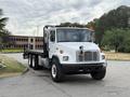 A white 1998 Freightliner FL80 truck with a flatbed and black side rails is parked, featuring a prominent front grill, multiple orange clearance lights, and large tires