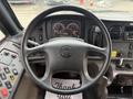 The steering wheel and control panel of a 2022 Freightliner B2 with gauges buttons and a thank you mat on the floor