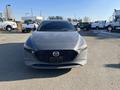 A gray 2023 Mazda MAZDA3 with a distinctive front grille and sleek design is parked with dirt on its surface