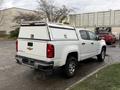 A white 2019 Chevrolet Colorado pickup truck with a cargo cap on the bed parked at an angle showing the rear and side views