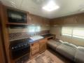 Interior of a 2014 Launch 24RLS travel trailer featuring a kitchenette with a stove microwave and sink along with a grey couch and wooden cabinetry