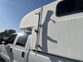 A white 2014 Ford F-350 SD with a camper shell featuring a ladder and mounting hardware attached to its side