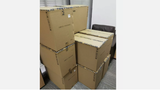 A stack of large cardboard boxes marked with logos and text, likely containing a Bitmain Antminer L9 ASIC miner for cryptocurrency mining