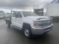 A white 2015 Chevrolet Silverado 3500HD with a flatbed and chrome grille parked at an outdoor location