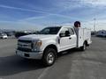 A white 2017 Ford F-350 SD with a service utility body and a mounted reel on the bed is parked in an outdoor area