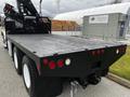 A 2006 Freightliner M2 112 flatbed truck with a black wooden loading surface and visible tail lights, showcasing its rear and towing equipment