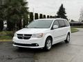 A 2017 Dodge Grand Caravan in white with a sleek design parked on a wet surface with visible windows and alloy wheels