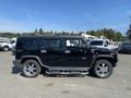 A black 2003 Hummer H2 with a shiny exterior and chrome accents parked on a lot displaying its distinctive boxy design and large wheels