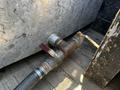 A rusted valve connected to a hose and metal piping attached to a vehicle, with a partially visible wooden structure nearby