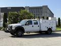 A white 2015 Ford F-550 truck with a flatbed and utility compartments on the side is parked with a front-mounted winch and visible lights on the roof