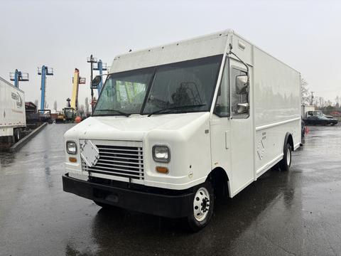A white 2012 Ford Econoline truck with a boxy shape and large front windows parked with wet surfaces reflecting nearby equipment and vehicles
