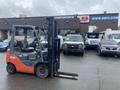 A 2011 Toyota 028FG15 forklift with an orange and black design featuring a raised fork in the front and a driver's seat with controls visible