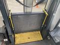 A metal wheelchair lift with a yellow safety bar in a vehicle designed for accessibility