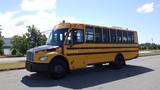 A 2014 Freightliner Thomas diesel school bus with a yellow exterior and black accents parked on a street