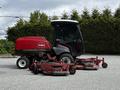 A 2012 Toro Groundsmaster with a red body and a black cab featuring two large rotary mowers attached at the front