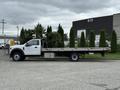A white 2022 Ford F600 flatbed truck parked with a flatbed longer than the cab and a side compartment for storage