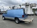 A blue 2010 Ford Econoline van with a large crane attachment and a bucket on the side mounted on a flatbed at the rear