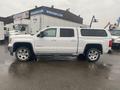 A white 2015 GMC Sierra 1500 truck is parked with a crew cab and a truck cap on the bed showcasing chrome wheels and a sleek design