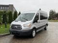 A silver 2019 Ford Transit van with large windows and distinctive grille parked on a wet surface