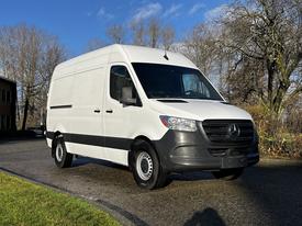 A white 2021 Mercedes-Benz Sprinter van with a black front grille and wheels parked on a paved surface