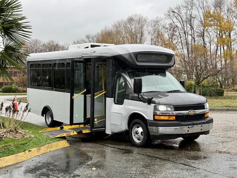 A 2019 Chevrolet Express bus with an open door and a wheelchair ramp extended for accessibility