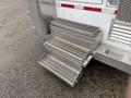 Three metallic steps with a diamond plate texture attached to the side of a vehicle with a red and white color scheme