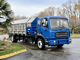 A blue 2017 Autocar Xpert truck with a flatbed and rear dumping feature is parked with its cab facing the viewer